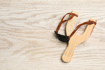 Slingshot with leather pouch on wooden background, top view. Space for text