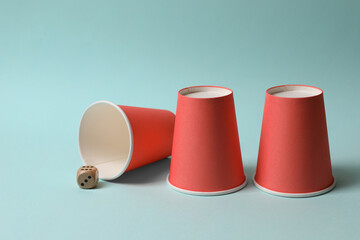 Three red cups and dice on light blue background. Thimblerig game