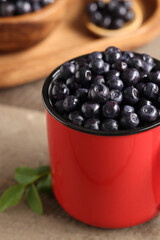 Red mug of tasty fresh bilberries on wooden table, closeup