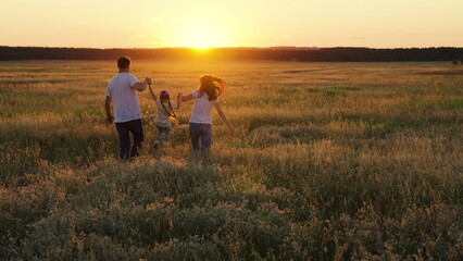 Fototapeta na wymiar Mother, father, child dream together in park at sunset. Family run on green grass in meadow. Happy family, child, walk through summer field, holding hands. Mom dad daughter walks together in nature.