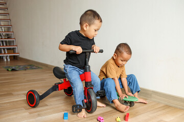 Two adorable Asian little kids playing together at home. Children playing with tricycle and...