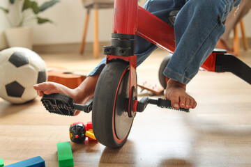 Cute little kid's foot cycling the tricycle pedal. Toodler using bike at home, close up.