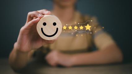 Customer review, customer service evaluation, and satisfaction concept. A businesswoman selects the smiley icon and gives five stars on a wooden block.