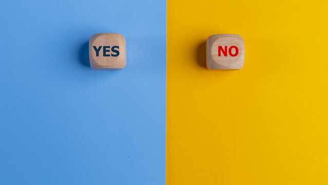 Wooden cube with yes and no text on a blue and yellow background. Business Choices For Difficult Situations, making Decisions.