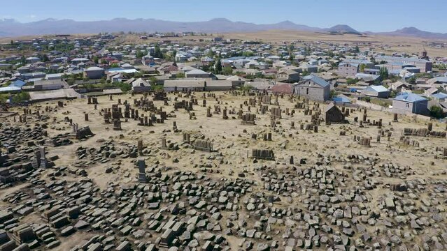 Forward reveal aerial shot of Noratus cemetery and the village on sunny summer day. Sevan lake, Gegharkunik Province, Armenia.