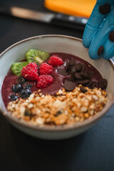 Preparation of delicious acai bowl with blueberry, raspberry, kiwi and chocolate chips.