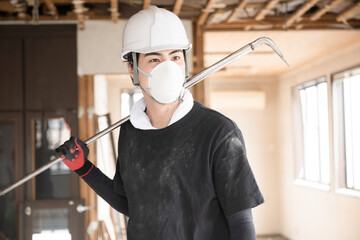 ヘルメットを被り作業着を着たバールを持つマスクの男性のアップの笑顔