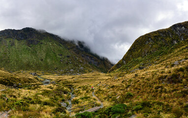Summit of the Routeburn mountain trail with a hiker and a river, New Zealand
