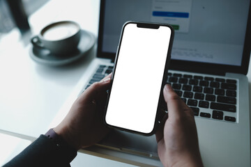 A man is sitting in a cafe, holding a blank screen mock-up mobile phone in one hand and a coffee cup in the other.