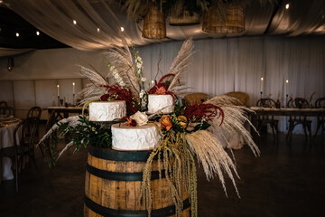 wedding cake at reception with pampas and florals in wicket baskets hanging from ceiling and wooden...