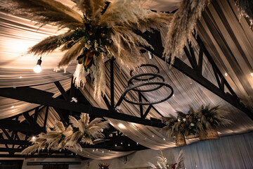 pampas grass and florals in wicker baskets hanging from black wooden beams at a wedding reception - obrazy, fototapety, plakaty