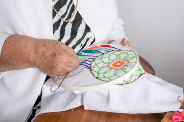 Manos de una anciana cosiendo, abuela bordando con hilos de colores