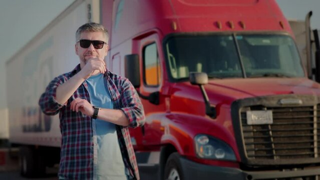 Professional Truck Driver approaches his red truck and Behind Him Parked Long Haul Semi-Truck 