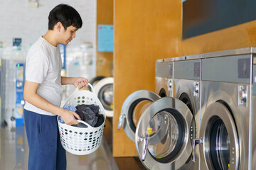 Asian man putting an used or dirty clothes in the self-service automatic laundry washing machine,...