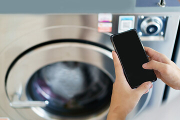 Isolated mockup black screen with clipping path. Asian man using self-service - automatic washing machine, Asian man using application on smartphone to access self service KIOS laundry machine.