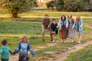 Obraz premium Large family of father, mother, two brothers and three sisters standing and sitting on a green field in summer, full length portrait.
