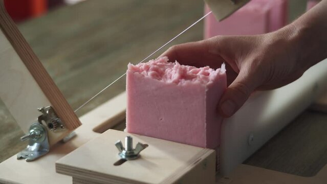 A woman master soap maker cuts handmade lavender soap on a wooden string cutter. Home production of natural cosmetics