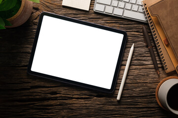 Top view of digital tablet with empty screen, coffee cup, notebook and keyboard on wooden table.