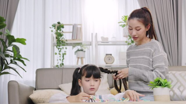 Mother brushing daughters hair on sofa at home .