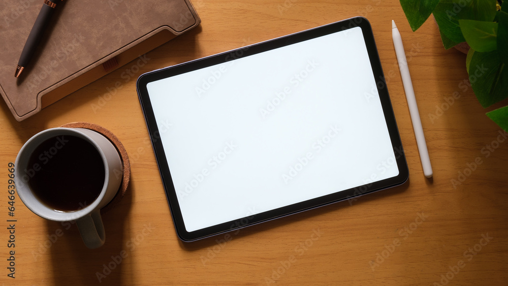Poster top view of digital tablet with empty screen, coffee cup, notebook and keyboard on wooden table.