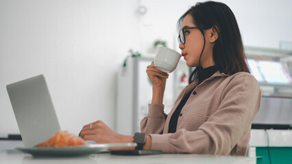 Asian business woman working on a laptop while enjoying a cup of coffee in a cafe
