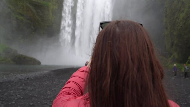 The girl photographs a large waterfall. Iceland.