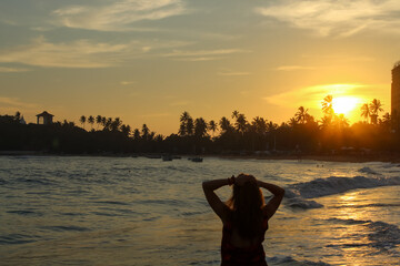 Silhouette of a woman enjoying the magical sunset at the beach of Unawatuna