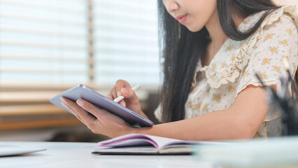 Cropped shot of young woman wearing using stylus pen writing notes on digital tablet.