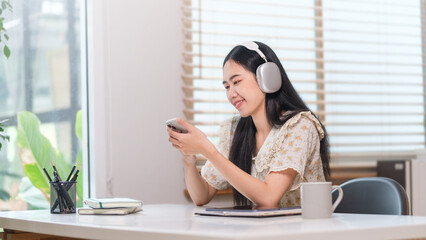 Obraz premium Cheerful Asian woman wearing headphone and use smart phone.