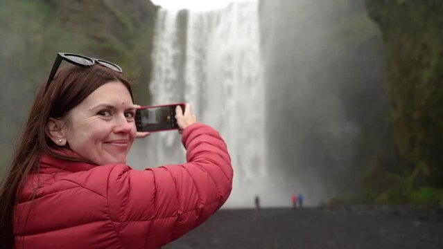The girl photographs a large waterfall. Iceland.
