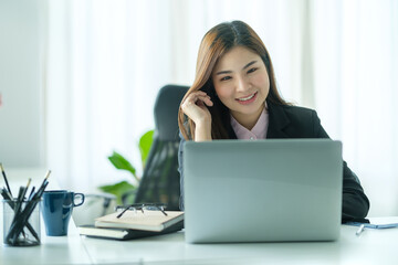 Attractive asian businesswoman in black suit sitting at office desk and using laptop computer.