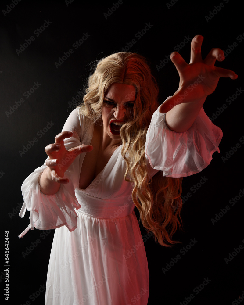Wall mural Close up portrait of scary blonde  vampire bride wearing elegant  white halloween fantasy gown. Isolated on dark  studio background with angsty gestural hands reaching out  - Wall murals