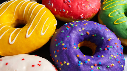 Purple, red, yellow, green and white donuts are on a black table. Close-up. Sweet delicious dessert.