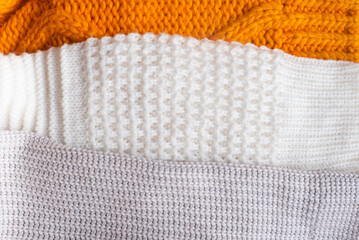 Handmade orange and white chunky knit sweaters lie against a background of textured linen.