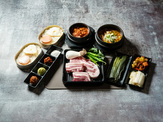 A set of various parts of raw pork, side dishes, and stew