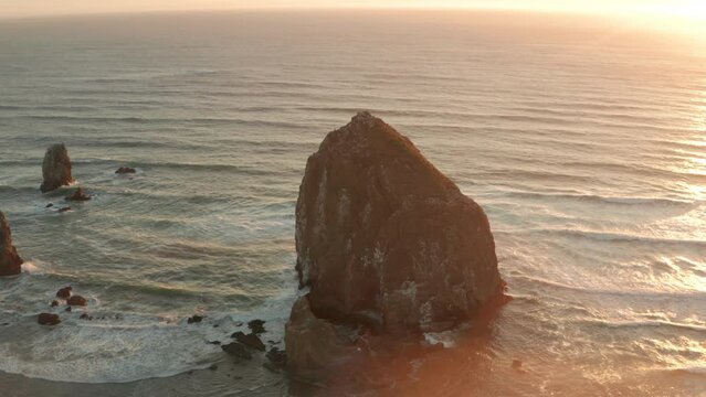 Circling aerial shot of Haystack rock sea stack at sunset