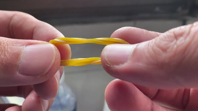 Male hands showing a rubber band and pulling elastic tugging on a rubber band between hands close up shot at home daytime