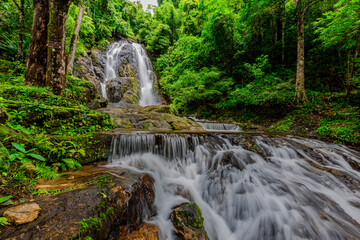 Fototapeta premium Background of a natural waterfall with cool water flowing from high mountains, Punyaban Waterfall Lamnam Kraburi National Park in Ranong Province, Thailand