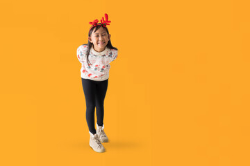 Fototapeta na wymiar Cheerful young Asian girl wearing a Christmas sweater with reindeer horns, Happy smiling standing posing full body portrait, isolated on yellow background