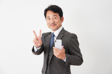 スマホを持ってピースサインをする中年のビジネスマン　白背景
