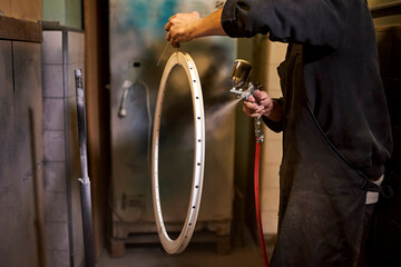 Unrecognizable person spray painting a bicycle rim in his bike workshop.