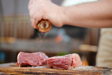 Unrecognizable man seasoning raw beef steak with pepper