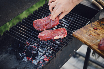 Unrecognizable man put raw strip steaks on hot grill