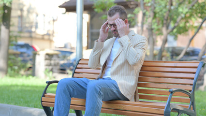 Tired Middle Aged Man Sitting Outdoor with Headache