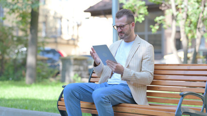 Middle Aged Man Upset by Loss on Tablet while Sitting Outdoor on a Bench