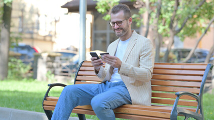 Obraz premium Middle Aged Man Doing Online Shopping via phone while Sitting Outdoor