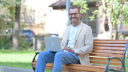 Middle Aged Man Smiling at Camera while Working on Laptop Outdoor