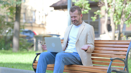Middle Aged Man Shocked by Loss on Laptop Outdoor