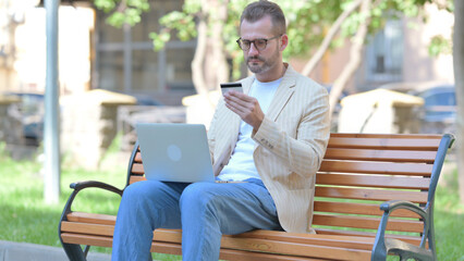 Middle Aged Man Excited for Successful Online Shopping on Laptop Outdoor