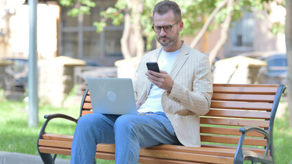Middle Aged Man Working on Laptop and Smartphone